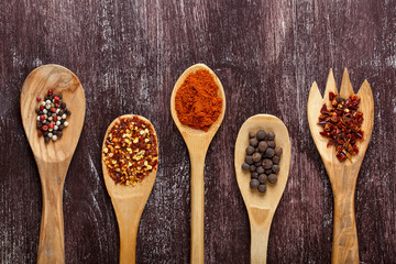 Various spices in wooden spoons on dark brown background. Different types of paprika and peppercorn.