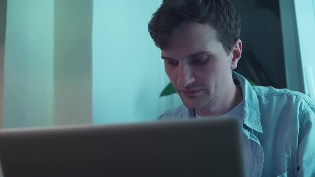 Man typing on notebook computer sitting near window