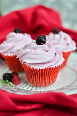 Three pink capkake with blackberries on the peak.