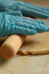 Pastry being rolled with a wooden rolling pin by a person wearing gloves