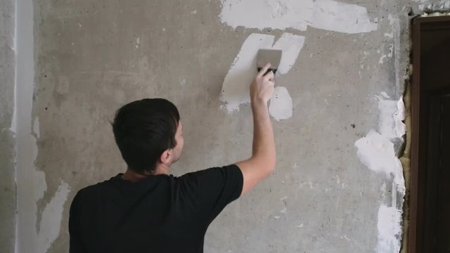 Man cleans the spatula pieces of wallpaper from beton wall