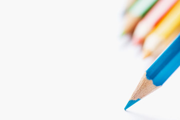 Row of Multicolored Pencils in Background Single Blue Sharp Pencil Pointing with Tip to Blank White Paper. Beginning of Drawing. Creativity Graphic Design Crafts Kids School Concept. Copy Space