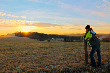 Naklejka na ściany i meble Young man in jacket looking to famous witer sunrise on Czech countryside