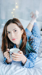 Happy woman relaxing home dressed in blue dots pyjamas drinking hot tea