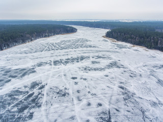 Flight over frozen lake breaking ice in rural village, Lithuania. Aerial photography during winter season.