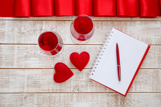 Valentines Day background with hearts and glasses of wine over white wooden table