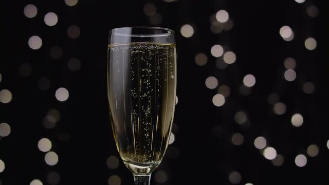 Glass of champagne with a rotating bubbles inside. Bokeh background