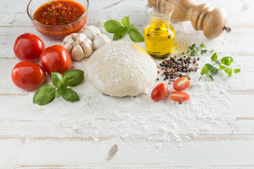Food ingredients and spices for cooking, tomatoes, oil, pepper, salt, garlic, basil, oregano and delicious italian pizza dough with napkin, fork and spoon on white wood background. Top view.