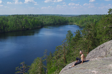 Fototapeta premium man sitting on cliff relaxing, above the lake Yastrebinoye, Priozersky district, Leningrad region, Russia