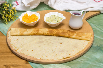 Rolled crepe, Russian blini on wooden cutting board with appetizers made with carrot and zucchini, and syrup