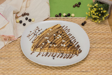 Folded crepe, Russian blini with chocolate sauce on white plate, chocolate chips on topping and...