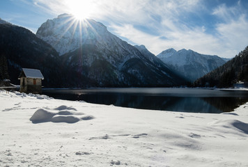 scenic mountain pass lake lago del predil with house in winter scenery with sunlight blue sky, italy