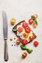 Open sandwiches rye bread with cream cheese and strawberry, basil, hazelnuts, tomatoes on old black metal wooden  surface. Healthy snack concept. Top view.