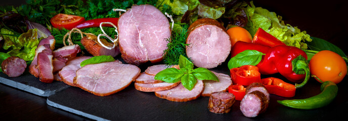 Smoked sausage, ham with red and green peppers and herbs on a dark background