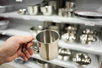 The buyer's hand of a man with a steel bowl on the background of a rack with utensils made of steel