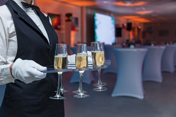 the waiter holds glasses with champagne on a tray