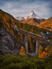 Scenic autumn view on snowy Matterhorn peak with blue cloudy sky , bridge and Gornergrat tourist train in Zermnatt, Switzerland.