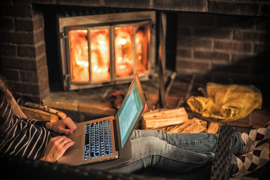 Woman working with a laptop at the warmth of the fireplace.
