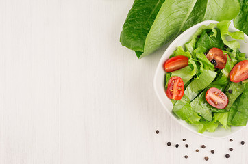 Spring fresh salad of green spinach and cherry tomato slices on white wood background, top view, copy space.