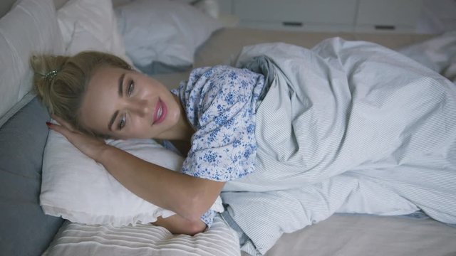 Charming young woman with ponytail lying on comfortable bed under soft blanket and sleeping peacefully. 
