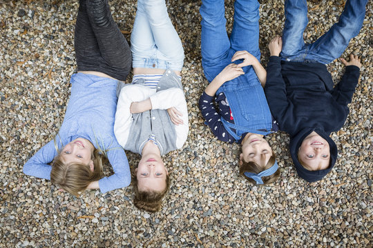 Three girls and a boy lying on the ground covered with pebbles