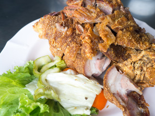 Crispy fried pork leg placed on a plate with vegetables and seasoning sauce