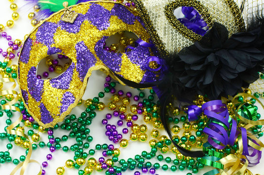 Mardi Gras image of close up detail of carnival masks, beads, ribbons and confetti in purple, green, gold and black on light background