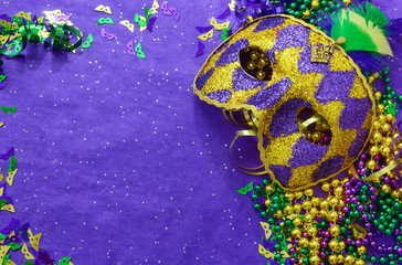 Mardi Gras border or frame of carnival masks, beads, ribbons and confetti in purple, green, gold and black on background of rough textured sparkly paper © Perry Correll