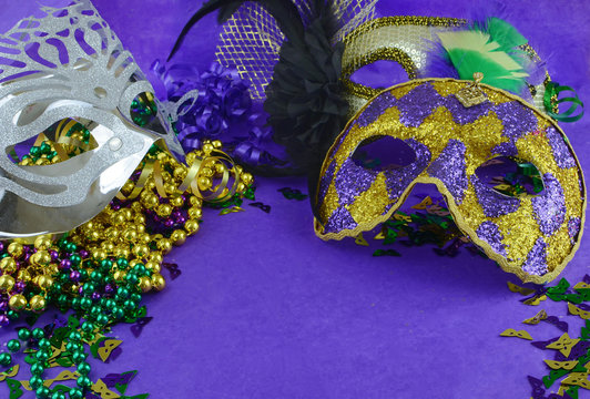 Mardi Gras border or frame of carnival masks, beads, ribbons and confetti in purple, green, gold and black on background of rough textured paper