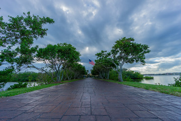 USA, Florida, Path of paver through alley of ancient trees between water with flag of usa behind