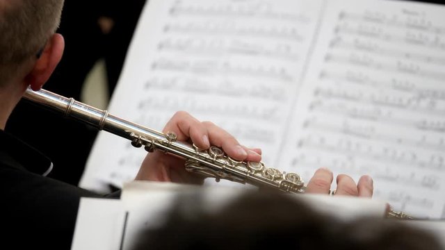 A shot of a musician playing on his flute and looking into music notes in front of him...