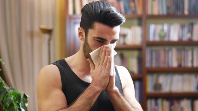 Young man blowing nose with handkerchief, indoor at home in his living room