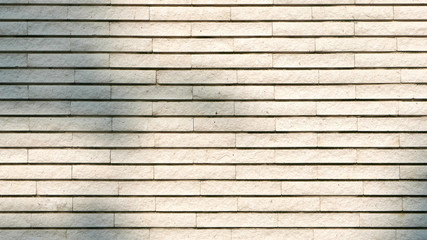 Horizontal textured wall of exterior building with tree shadow