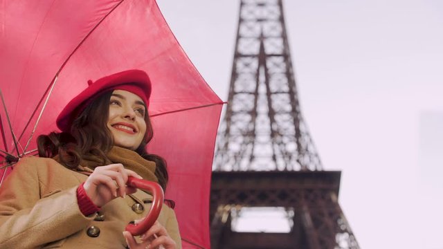 Happy lady standing under umbrella smiling to passers-by waiting for her friend