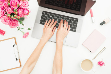 Home office desk. Woman workspace with female hands, laptop, pink roses bouquet, accessories, diary on white. Top view. Flat lay. Girl working on laptop.