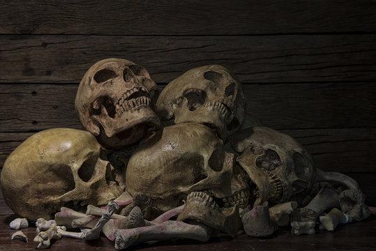 Human skulls and pile of bones are laid on old wooden floors and background on a night where the atmosphere is scary and dim  lights. Halloween night, Life and death concept. Still life style, art.