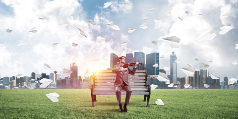 Handsome violinist in park on wooden bench play his melody