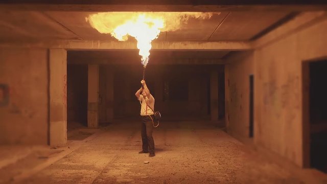 Yong male artist performing fire show via flamethrower at dark in slow motion.