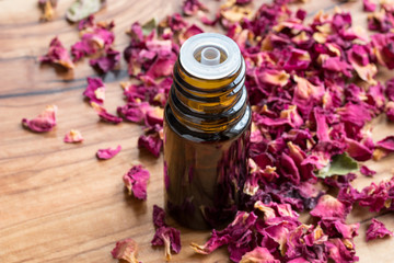 A bottle of rose essential oil with dried rose petals on a wooden background
