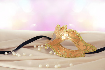 Image of elegant gold venetian mask over delicate silk fabric background.
