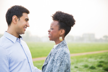 Side view of young smiling couple who standing in embrace and looking at each other outdoors