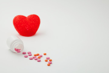 pills poured from a bottle and heart on a white background