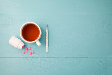 thermometer, tablets and tea on a blue background