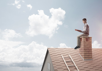 Handsome man on brick roof against cloud scape reading book