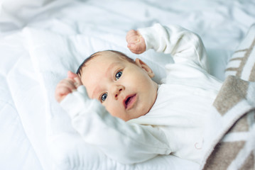 Cute funny baby lying on a white bed covered with a blanket. Concept of The tenderness of motherhood and family values