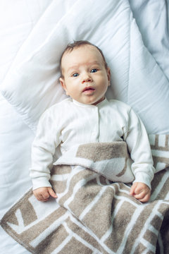 Cute funny baby lying on a white bed covered with a blanket. Concept of The tenderness of motherhood and family values