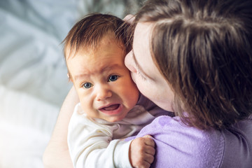 Happy caring mother holding a smiling baby boy and kisses him. Concept of the tenderness of motherhood and family values