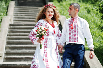 Obraz premium Lovely couple in ukrainian traditional embroidered clothing walk down the stairs with a bouquet.