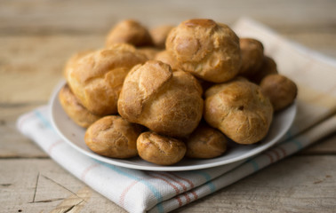 Isolated profiterole on a white plate on a dishcloth on a wooden table, 