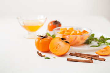 Chopped ripe persimmon in a bowl with cinnamon sticks on white table